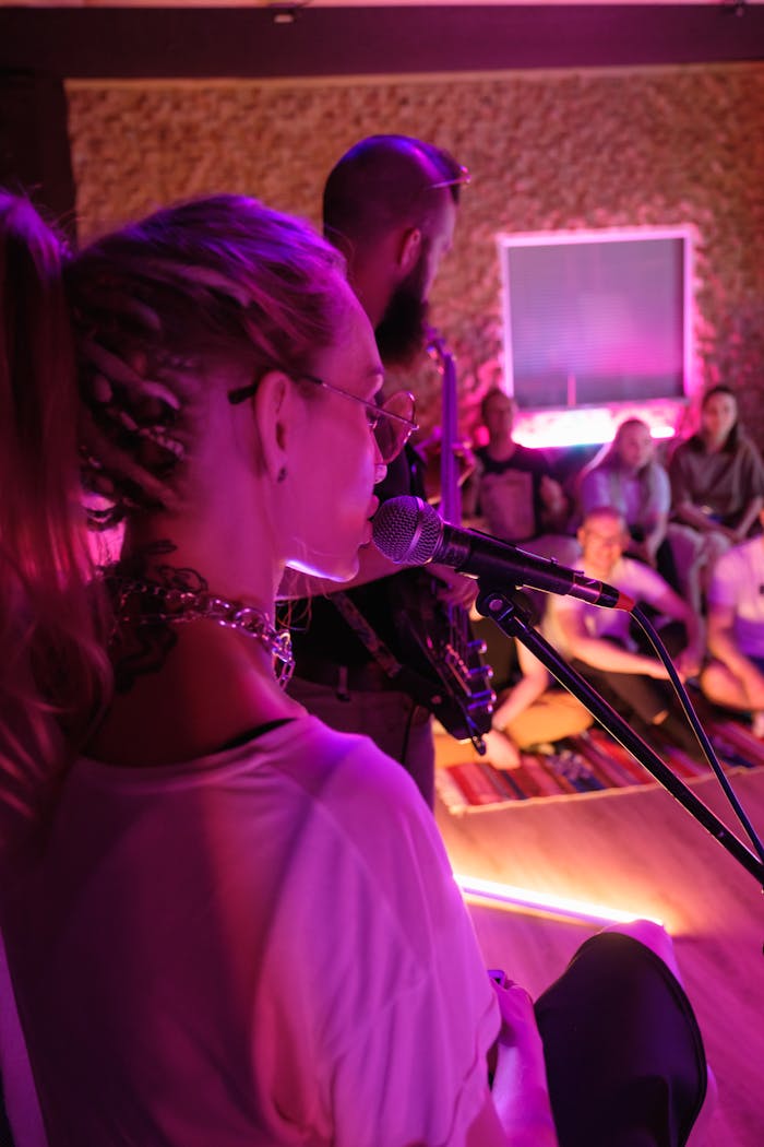 A close-up of a female singer performing live with an audience in a cozy indoor setting.